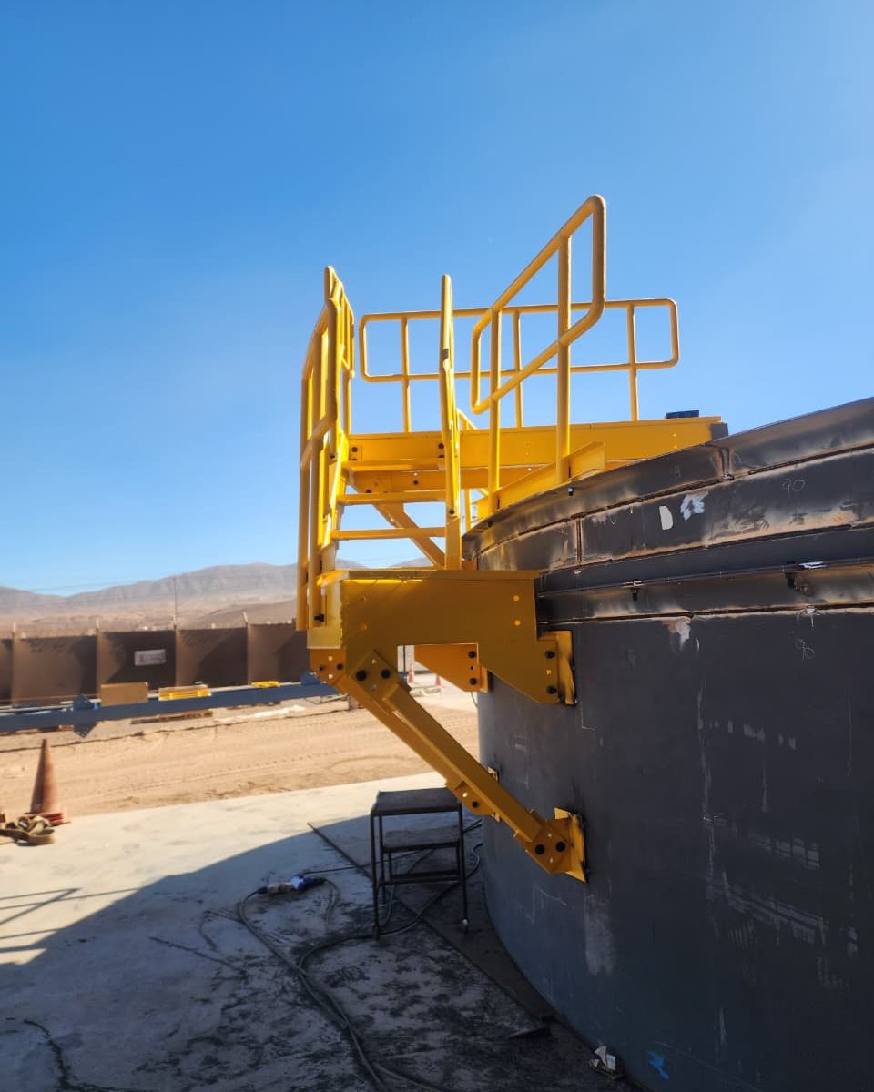 Plataforma y barandas amarillas montadas sobre el borde del techo del estanque, con el desierto de fondo